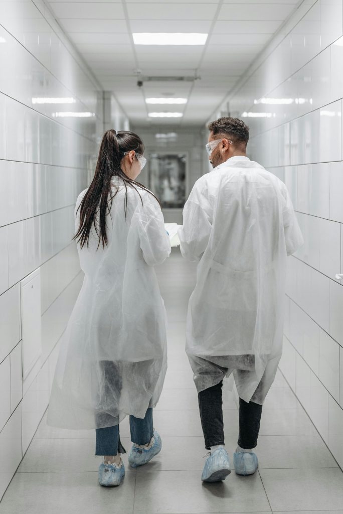 Researchers in lab coats and goggles walking through a laboratory hallway, engaging in teamwork.